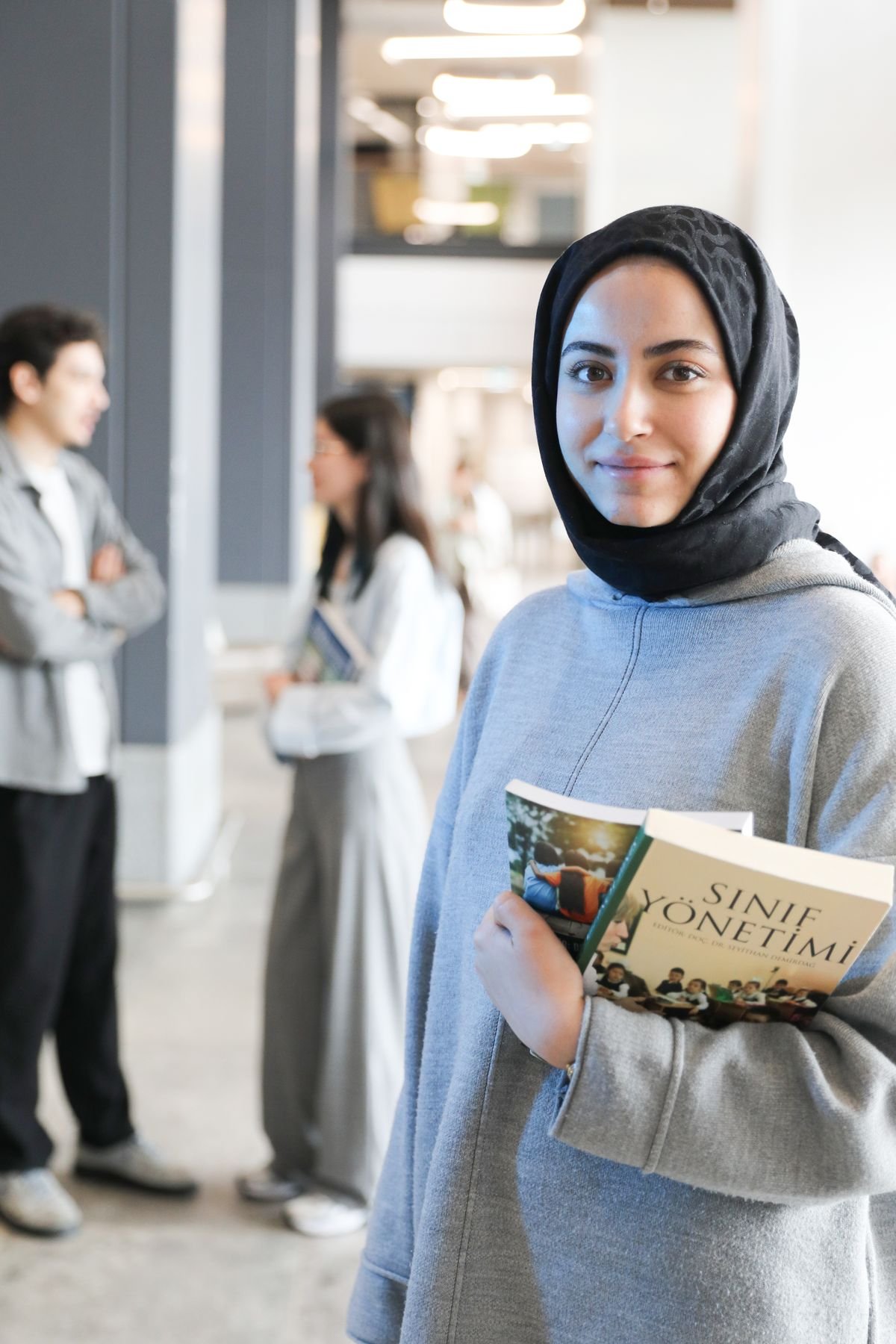 طالبة تبتسم وهي تحمل كتابها في ردهة الجامعة
